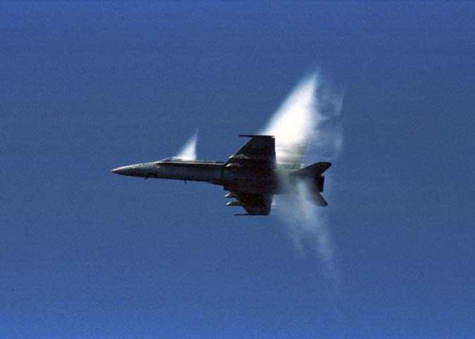 an f18 hornet flys above the uss kitty hawk aircraft carrier